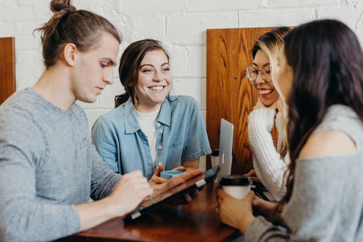 Vier Menschen sitzen mit Kaffeebechern an einem Tisch und lachen