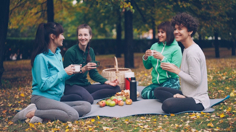Vier Frauen sitzen auf einer Decke bei einem Picknick in einem herbstlichen Park