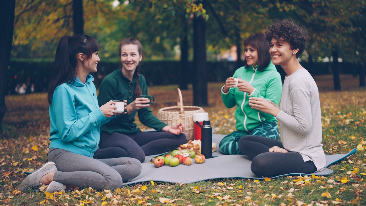 Vier Frauen sitzen auf einer Decke bei einem Picknick in einem herbstlichen Park